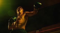 a shirtless man wearing boxing gloves and holding a punching glove in his right hand