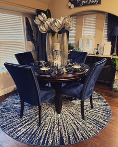 a dinning room table with blue chairs and flowers in vases on the rug