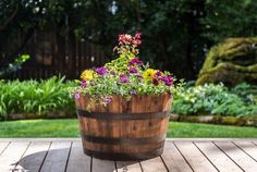 a wooden barrel filled with lots of flowers on top of a wooden table in front of some trees