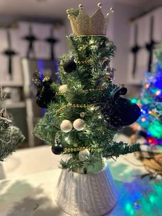 a small christmas tree decorated with ornaments and lights in a white ceramic pot on a table