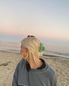 a woman standing on top of a sandy beach next to the ocean with her hair in a bun