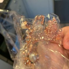 a person is holding some gold and silver beads in their hand while they are wrapped in plastic