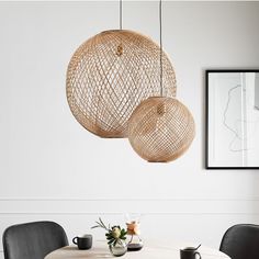 two wicker lamps hanging from the ceiling above a dining room table with black chairs