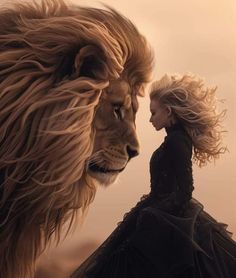 a woman standing next to a lion with her hair blowing in the wind, looking at it's face