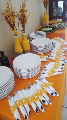 an orange table topped with white plates and silverware next to vases filled with yellow flowers