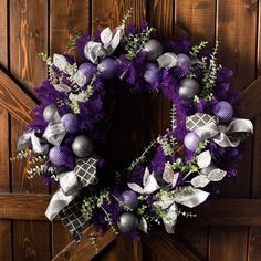 a wreath with purple and silver decorations hanging on a wooden wall next to a door