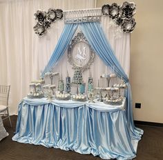 a table topped with cakes and cupcakes under a blue drape covered backdrop