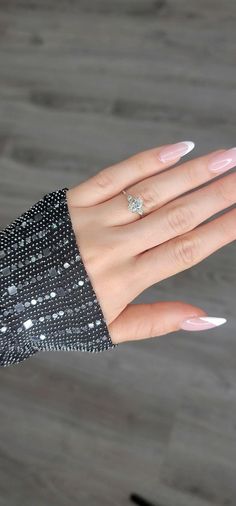 a woman's hand with white manicured nails and a diamond ring on it