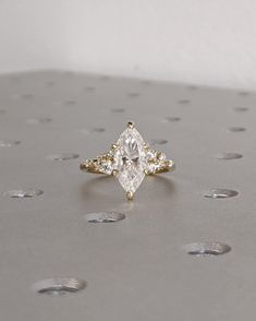 a diamond ring sitting on top of a silver surface with dots around it and the center stone is surrounded by smaller diamonds