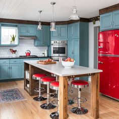 a kitchen with blue cabinets, red refrigerator and stools in front of the island