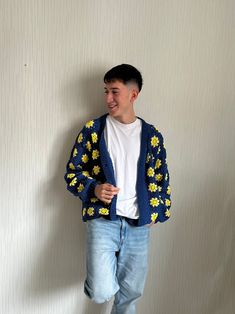 a man standing in front of a white wall wearing a blue and yellow cardigan