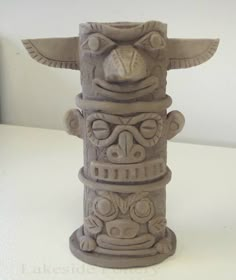 a ceramic tiki statue sitting on top of a white table next to a wall