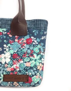 a blue floral purse with brown leather handles on a white background, the bag is made out of fabric and has a flower pattern