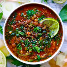 a white bowl filled with soup and garnished with cilantro, limes, and beans