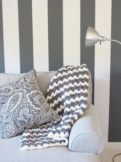 a couch with two pillows and a blanket on it in front of a black and white striped wall