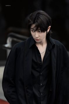 a young man with black hair and piercings wearing a black shirt is standing in front of a building