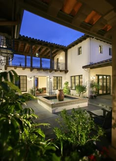 an outdoor courtyard with a fountain and potted plants at night, in front of a house