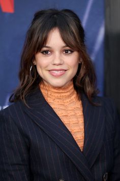 a woman in a pinstripe suit and turtle neck sweater smiles at the camera