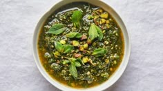 a white bowl filled with green soup and topped with fresh minty leaves on top