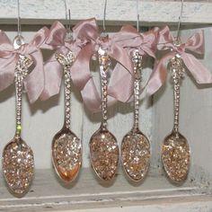 five spoons with glitter on them are hanging from a shelf next to a pink ribbon