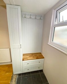 an empty room with a bench and coat rack on the wall, next to a window