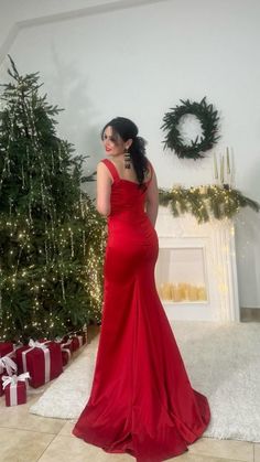 a woman in a red dress standing next to a christmas tree