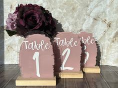 two pink wooden table numbers with a purple flower in the middle and one on each side