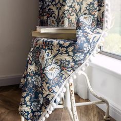 a blue and white chair with a book on it's back in front of a window