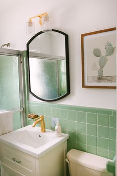 a bathroom with green tiles and a white toilet next to a sink, mirror and shower stall