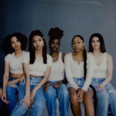 four young women sitting next to each other in front of a gray wall with their hands on their hipss