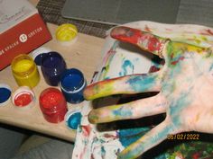 a person's hand covered in paint next to paints and other items on a table