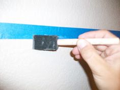 a person is holding a pencil and stamping something on the wall with blue tape