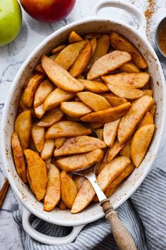 baked apples in a white casserole on a marble table with cinnamon and apple slices