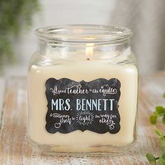 a candle is sitting on a table with some plants in the background and a chalkboard sign that says, mrs bennett