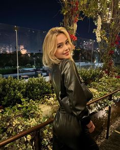 a woman in black leather dress standing on stairs at night with flowers hanging from the ceiling