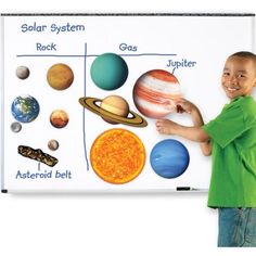 a young boy standing next to a white board with planets on it