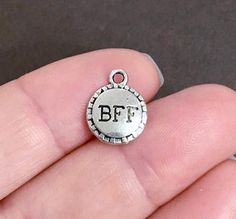 a person is holding a silver charm with the letter bf on it's side