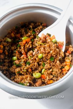 a bowl filled with rice and vegetables on top of a white tablecloth next to a spoon