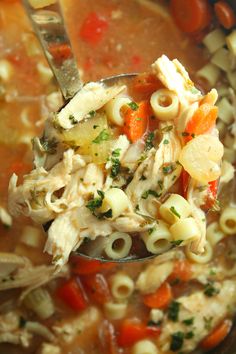 a spoon full of chicken noodle soup with pasta and carrots in it,