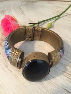 "Lovely vintage Cloisonné hinged brass bracket. Pink and blue floral designs. Large black celluloid stone embellishment. Decorative hinged closure. Very pretty. This bracelet was given to me by my sister who wore it in the 70s then stored it for years. It is in great vintage condition. Diameter is 2.5\", width is 0.5\". Remember: Vintage is never perfect. Each vintage item was owned and used for years before it was found and listed in this shop. Please see all photos as they are part of the desc Vintage Black Enamel Bracelet Jewelry, Vintage Black Enamel Bracelet, Vintage Adjustable Hinged Bracelet, Vintage Adjustable Hinged Cuff Bracelet, Vintage Adjustable Hinged Bracelets, Vintage Adjustable Hinged Bangle, Vintage Metal Hinged Cuff Bracelet, Vintage Metal Cuff Bracelet With Hinge, Vintage Black Bangle As Gift