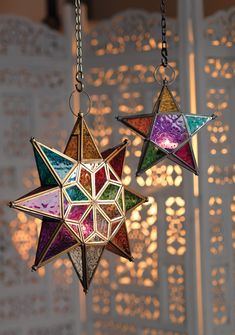 two multicolored stars hanging from chains in front of a white wall with laser cut screens