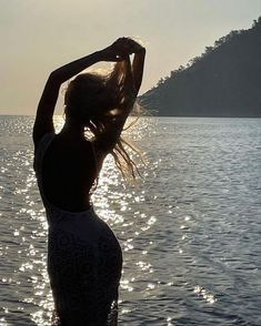 a woman is standing in the water with her hair blowing back and looking into the distance