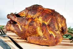 a whole chicken sitting on top of a cutting board next to a knife and fork