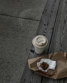 a cup of coffee sitting on top of a wooden table next to a brown paper bag