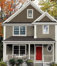 a gray house with white trim and red door in the front yard on a fall day