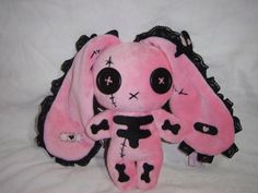 a pink stuffed animal with black lace on it's ears and eyes, sitting on a white sheet