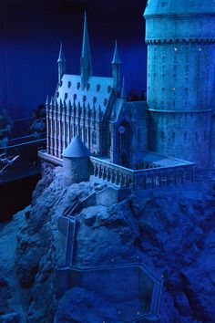 the hogwarts castle model is lit up at night with blue lights and people looking on