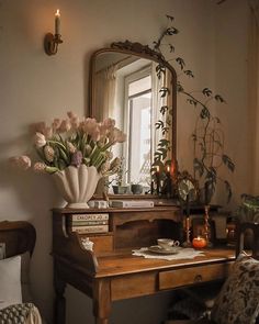 a wooden desk topped with a mirror next to a vase filled with flowers and candles