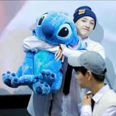 a man holding a blue stuffed animal in front of a person wearing a hat and tie