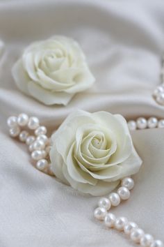 two white roses and pearls on a white cloth